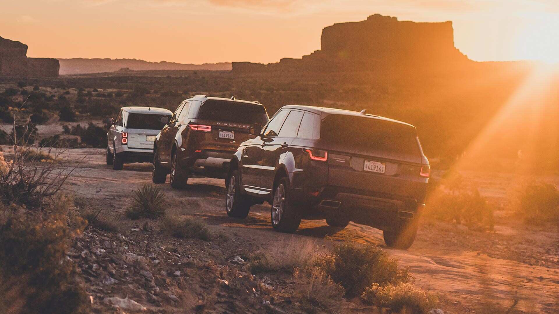 3 Land Rover vehicles driving over rocky ground as the sun sets