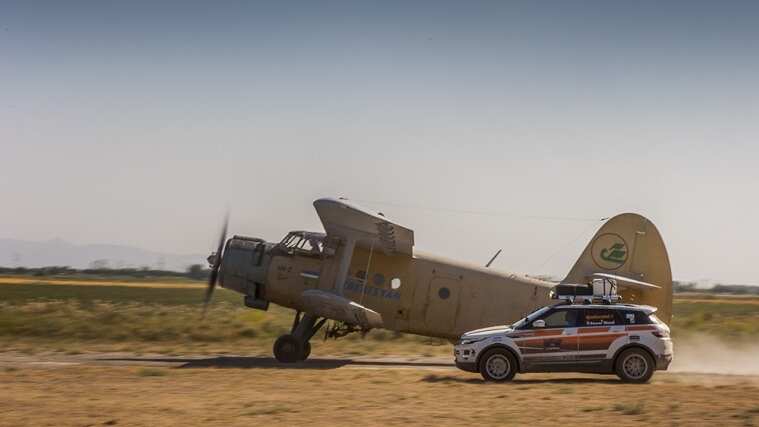 Land Rover driving on a dirt runway alongside aeroplane.